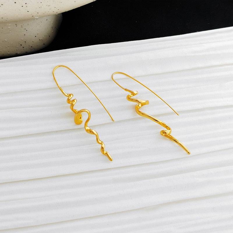 Serenity Threader Earrings in gold displayed on a textured white surface, emphasizing their stylish three-dimensional design. A perfect accessory for Memorial Day 2024.