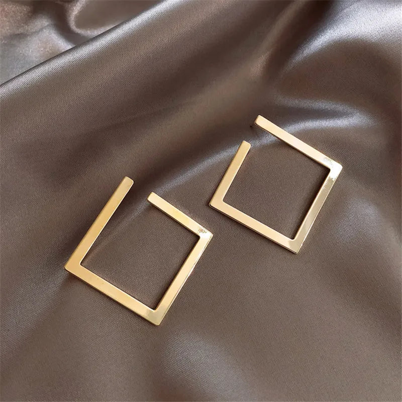 Modern vintage stud earrings in gold-tone with geometric square design, placed on satin fabric. Elegant and stylish drop earrings for women.