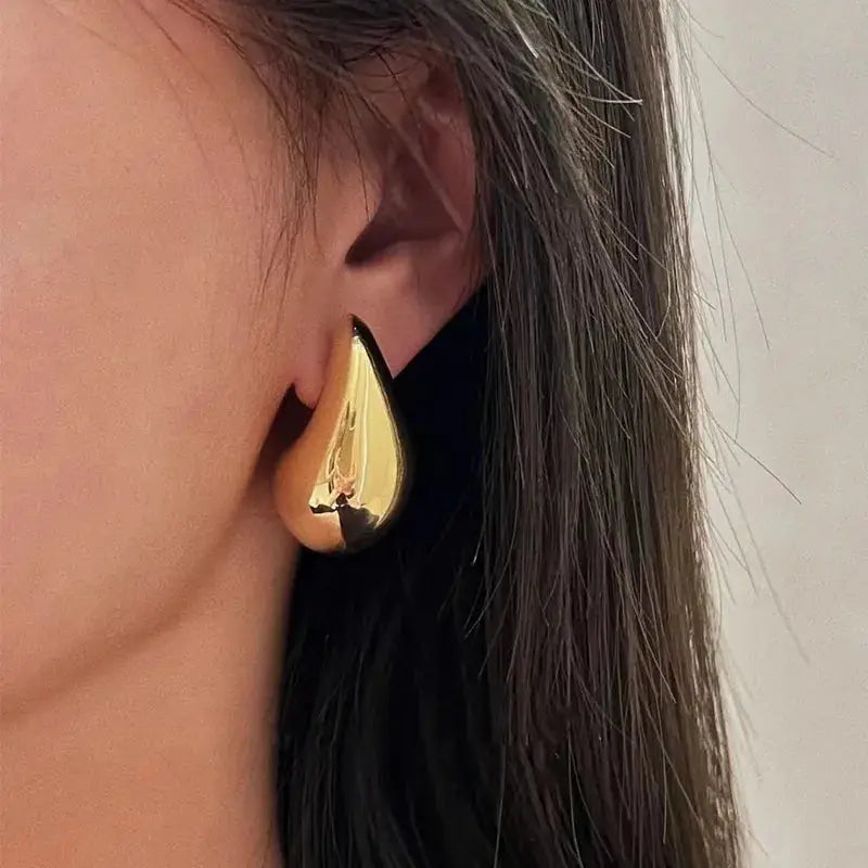 Gold teardrop-shaped earrings worn by a model, showcasing a sleek and minimalist design. A sophisticated jewelry piece.