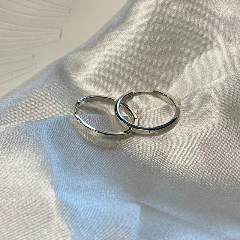 Silver-tone minimalist hoop earrings displayed on satin fabric. Classic and elegant modern vintage earrings for women.