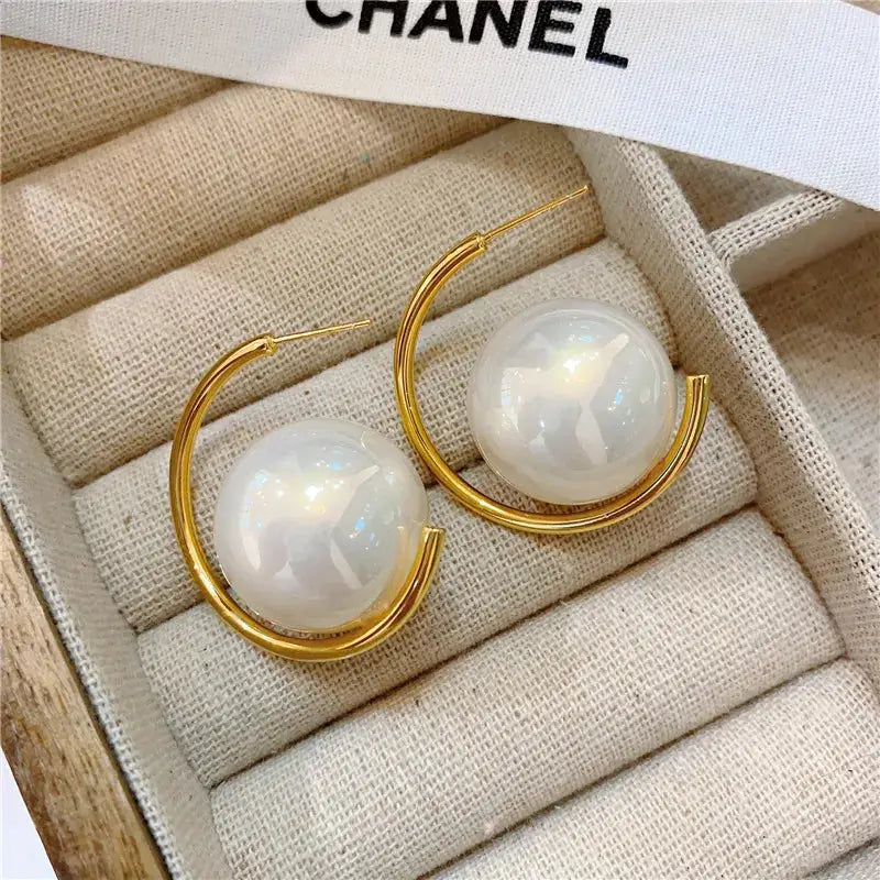 Gold hoop earrings with large pearl accents, displayed in a jewelry box. A luxurious and elegant accessory.