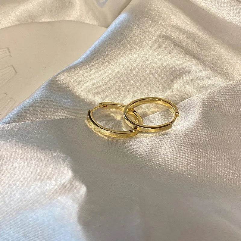 Gold-tone minimalist hoop earrings displayed on satin fabric. Timeless and elegant modern vintage earrings for women.