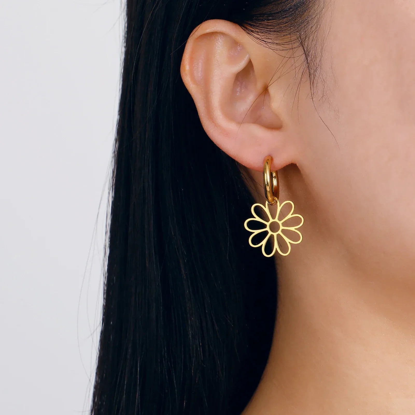 Model wearing gold flower hoop earrings with a single floral charm. Chic and minimalist jewelry piece for everyday elegance.