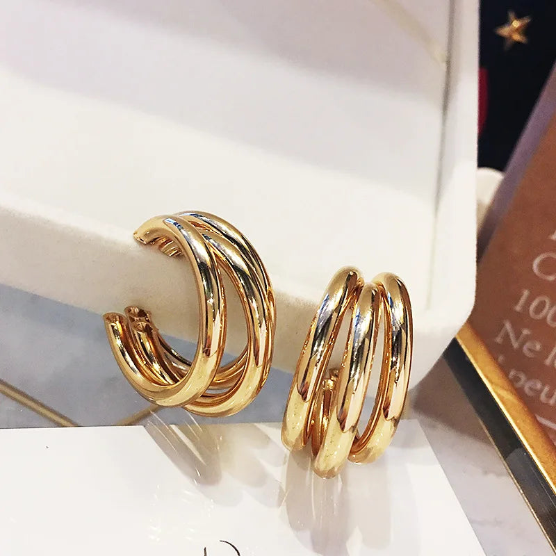 Gold-tone triple hoop stud earrings with a modern vintage aesthetic. Stylish and versatile metal earrings for women.