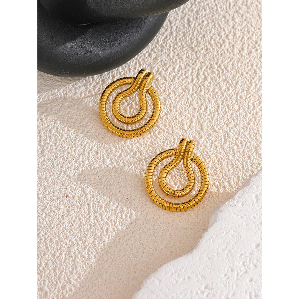 Gold-tone stainless steel geometric snake earrings displayed on textured surface. Vintage-inspired African symbol earrings for women.
