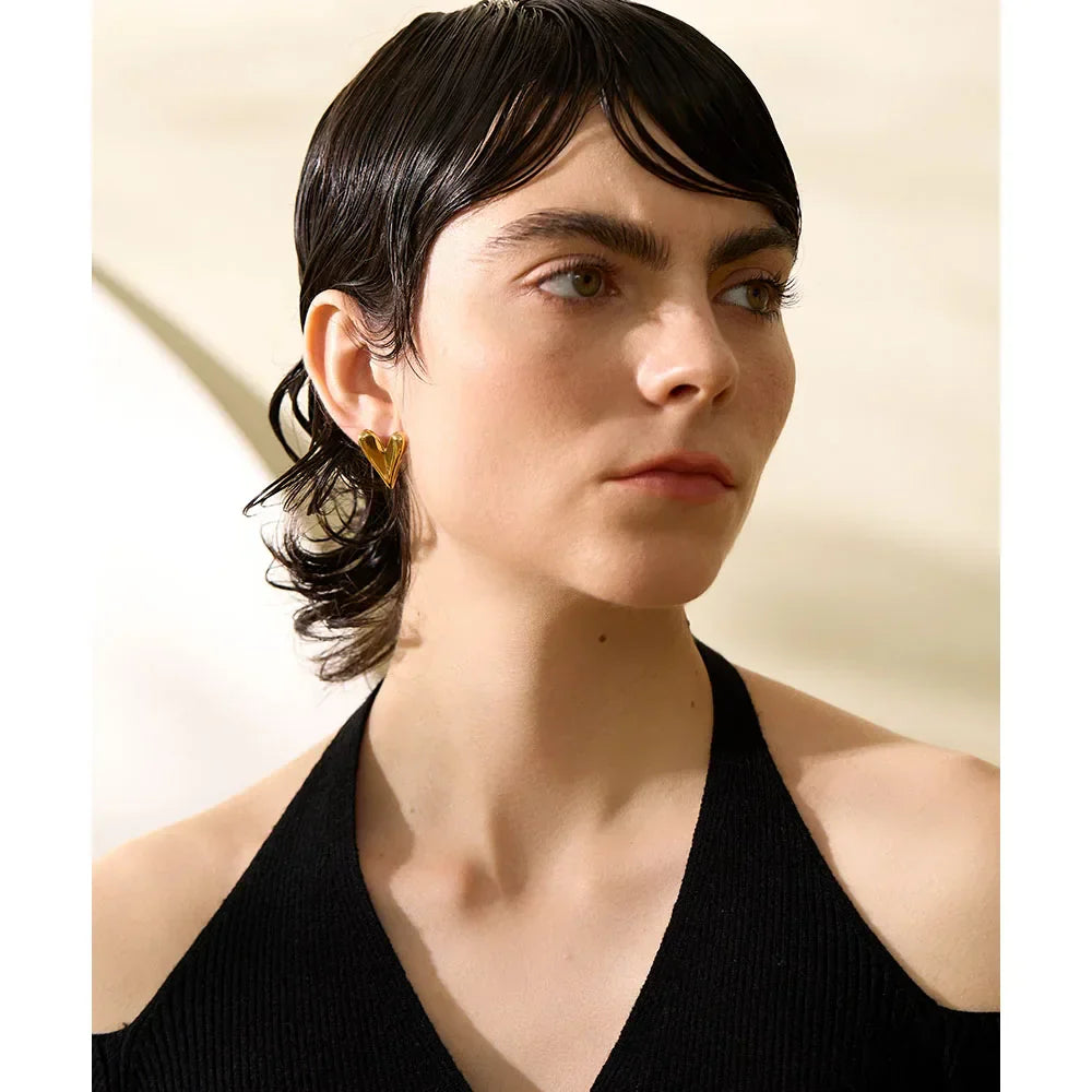 Model wearing gold stainless steel heart stud earrings, showcasing their bold and chic design. A trendy accessory for a sophisticated look.