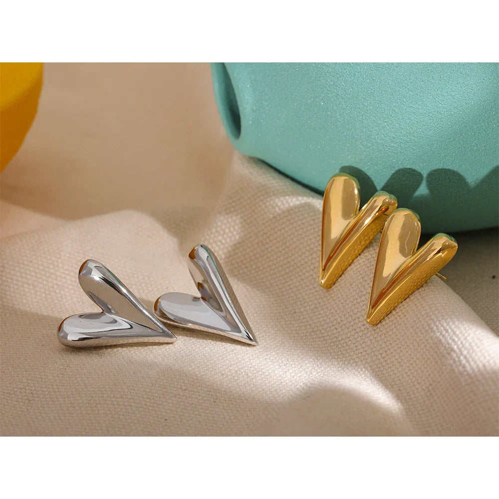 Gold and silver stainless steel heart stud earrings displayed on a neutral fabric background. A stylish and versatile jewelry choice for women.