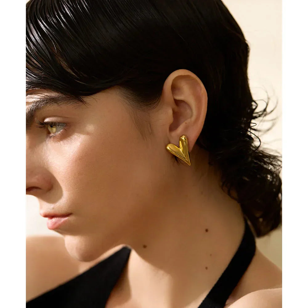 Close-up of a model wearing gold stainless steel heart stud earrings. A fashionable and elegant accessory for everyday or special occasions.