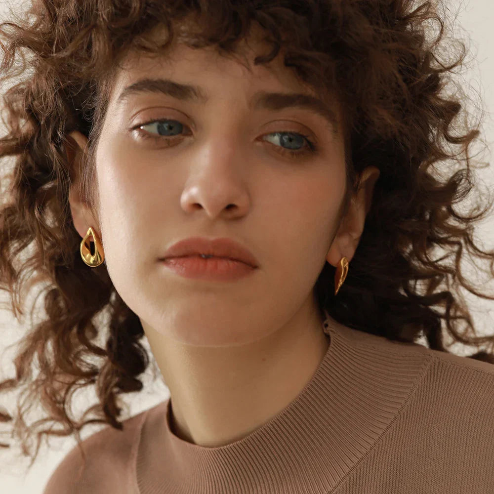 Close-up of model wearing gold stainless steel round hollow stud earrings. Chic and timeless accessory for women’s fashion jewelry collection.