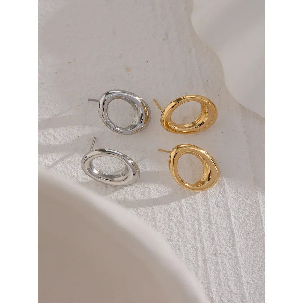 Gold and silver stainless steel round hollow stud earrings displayed on a textured surface. Minimalist and vintage-inspired jewelry for women.