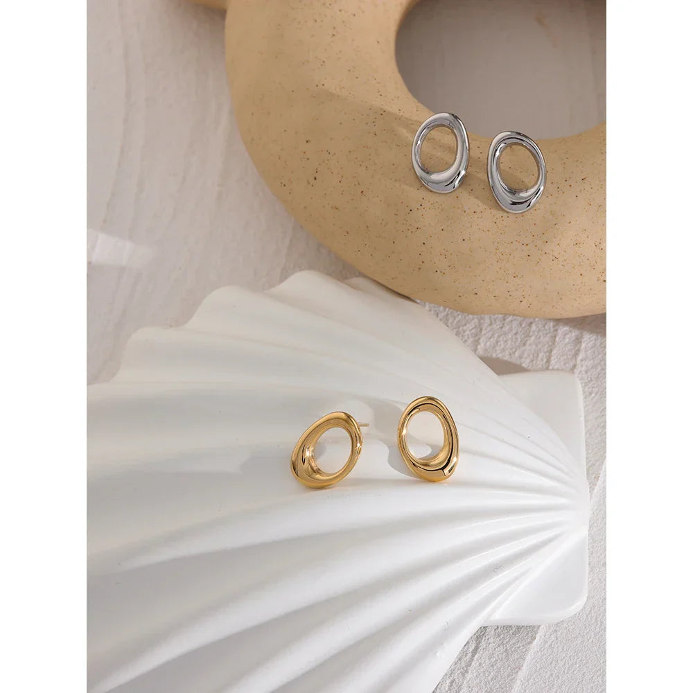 Gold and silver stainless steel round hollow stud earrings placed on decorative elements. Elegant and modern jewelry for women’s accessories.