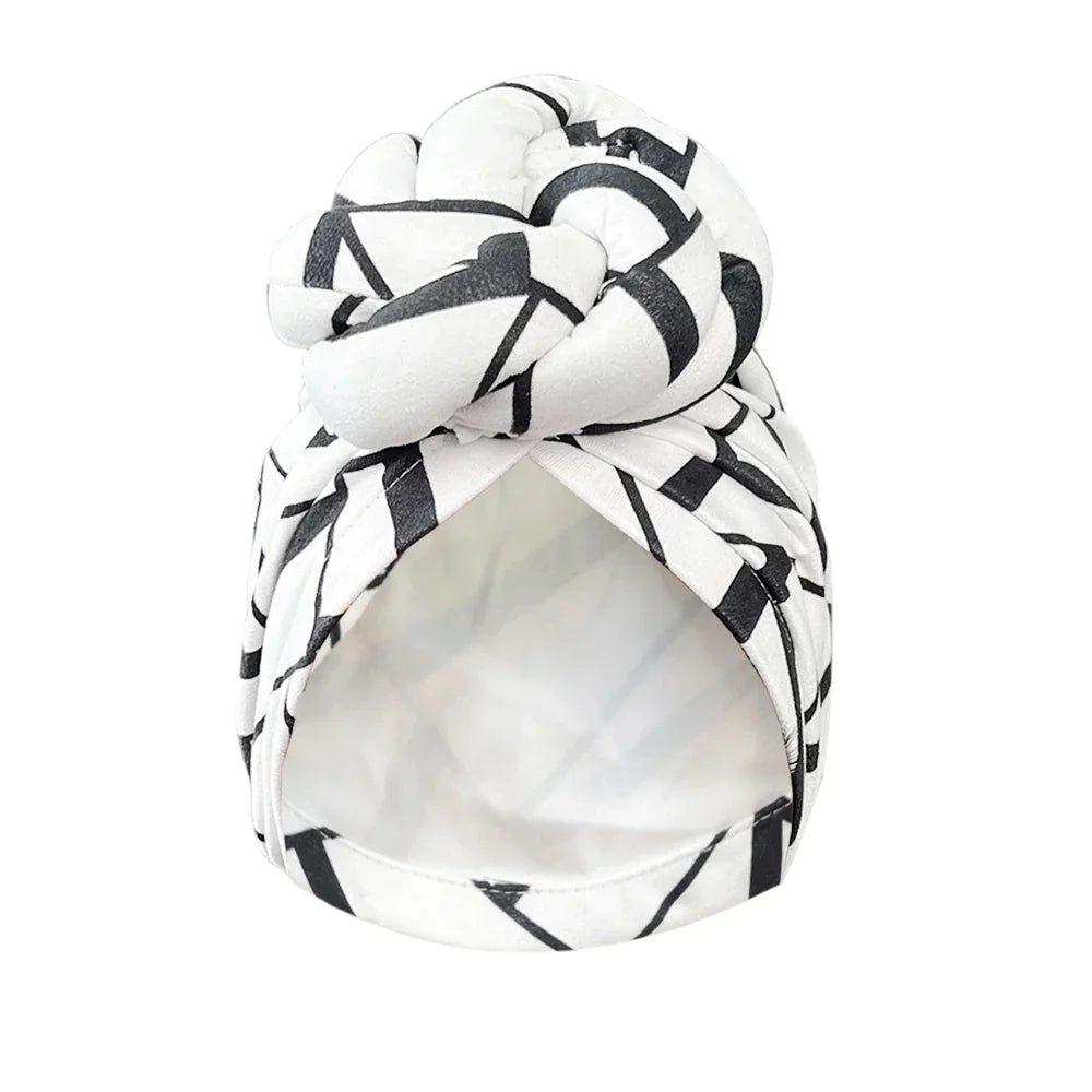 White and black patterned knot turban headwrap with a soft fabric and intricate geometric design, perfect for stylish headwear.