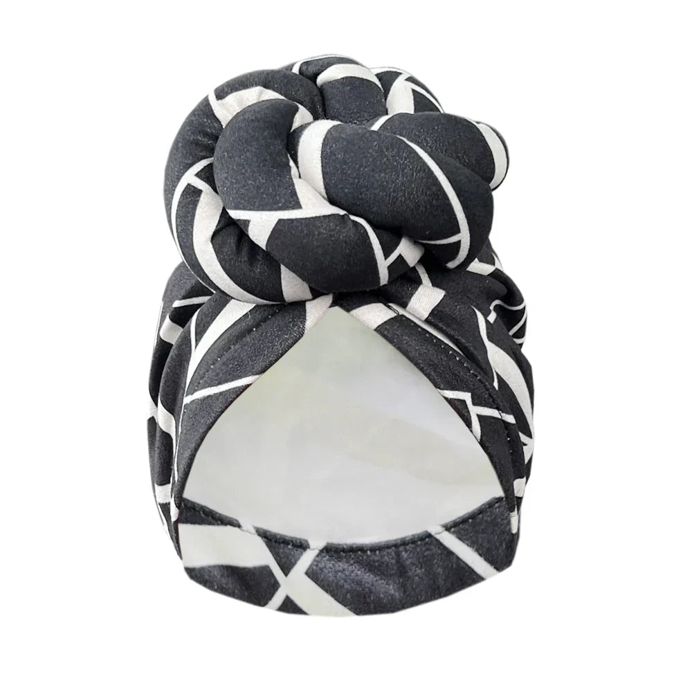 Black and white geometric patterned knot turban headwrap with a dark base, offering a sophisticated and stylish headwear option.