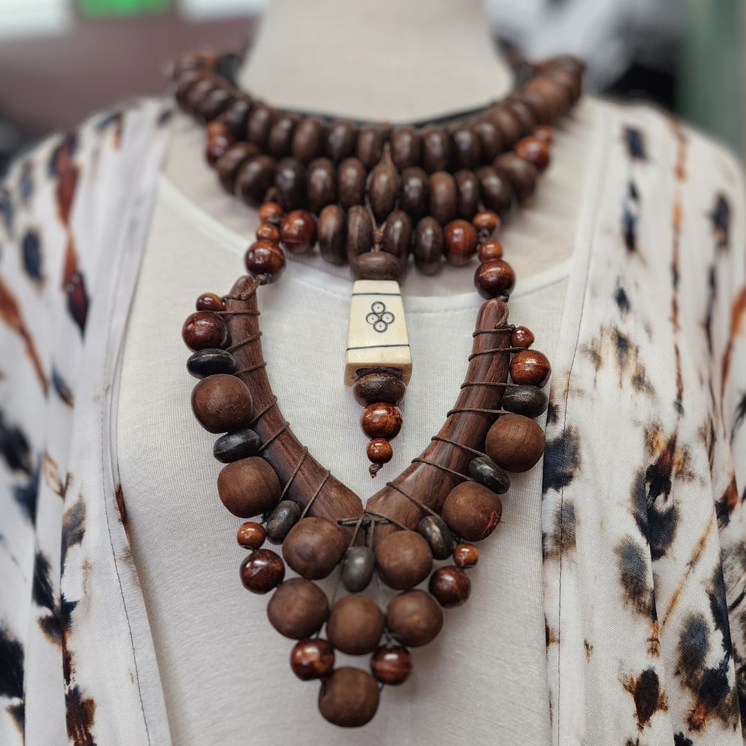 Handmade wooden beaded bib necklace with intricate tribal design, featuring dark brown beads and a central engraved pendant. A bold statement piece for bohemian and ethnic fashion styles.