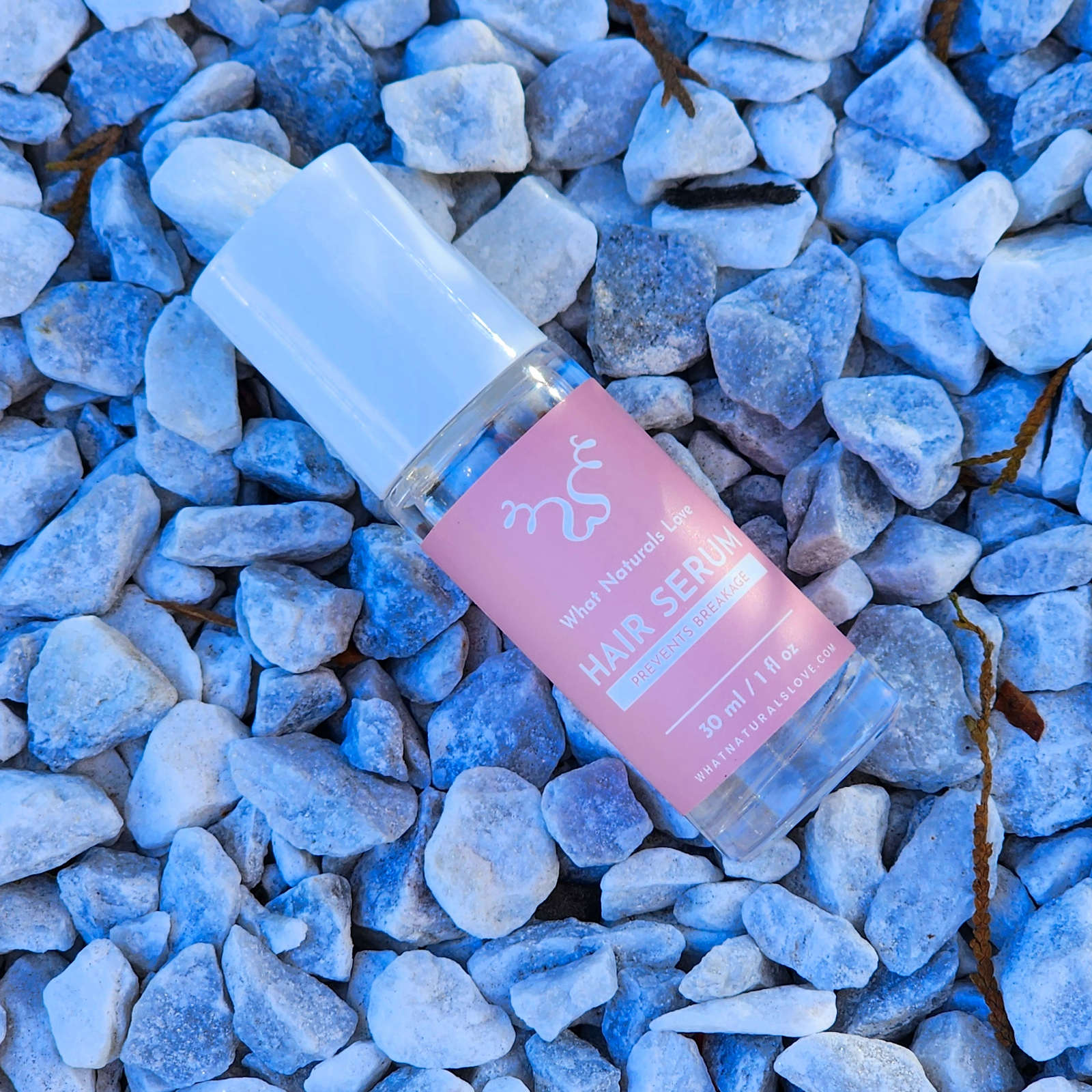 What Naturals Love Hair Serum bottle on white stones. Promotes hair growth, hydrates scalp, and strengthens locs with natural ingredients.