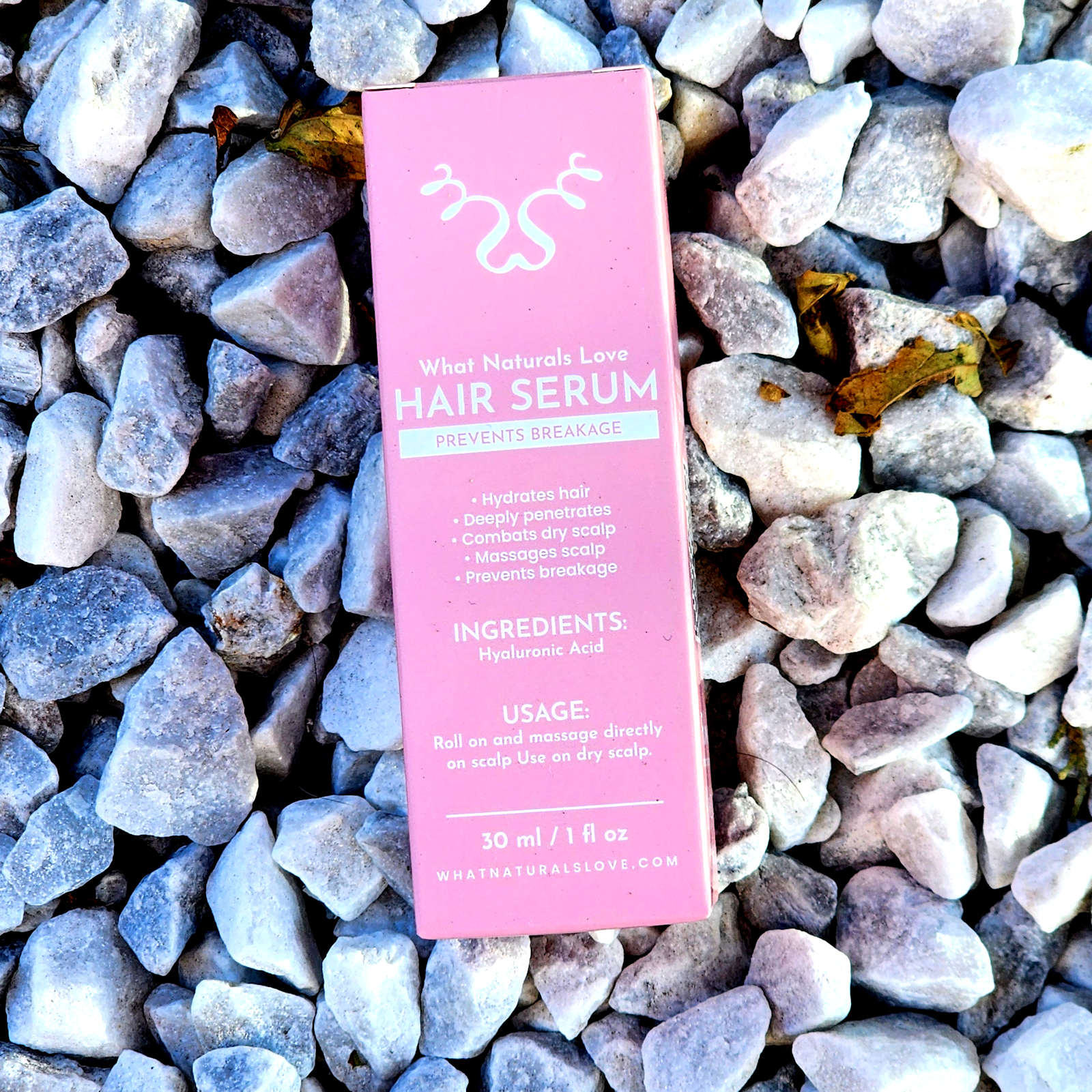 What Naturals Love Hair Serum packaging on white stones. Hydrates hair, combats dry scalp, and prevents breakage with hyaluronic acid.