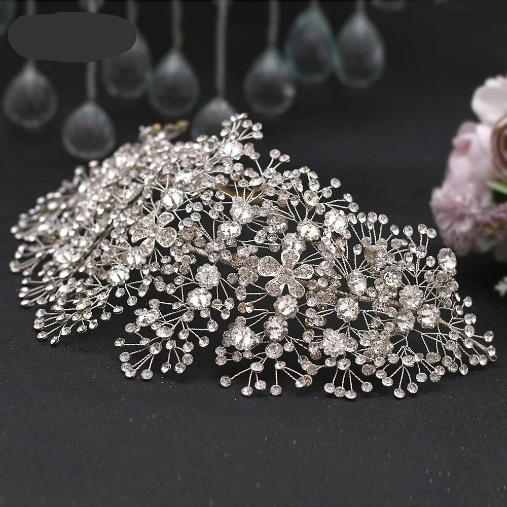 Silver floral rhinestone hairpiece displayed on black fabric with soft floral background.