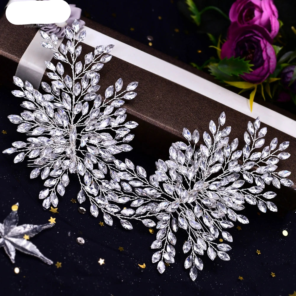 Silver bridal headpiece with leaf-shaped crystals displayed on a dark background with flowers
