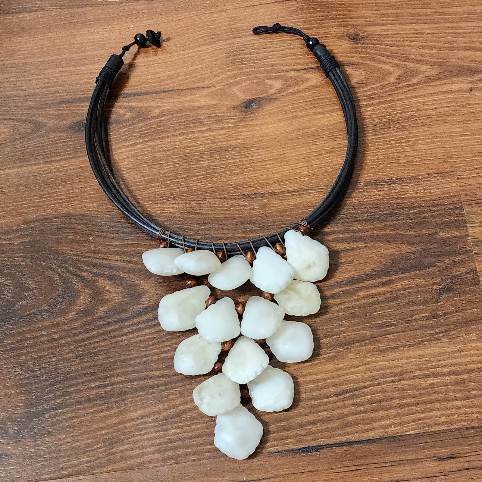 Ivory Petal Cascade Choker featuring handcrafted white stone-like beads on a black multi-strand cord. Elegant statement necklace for any occasion.