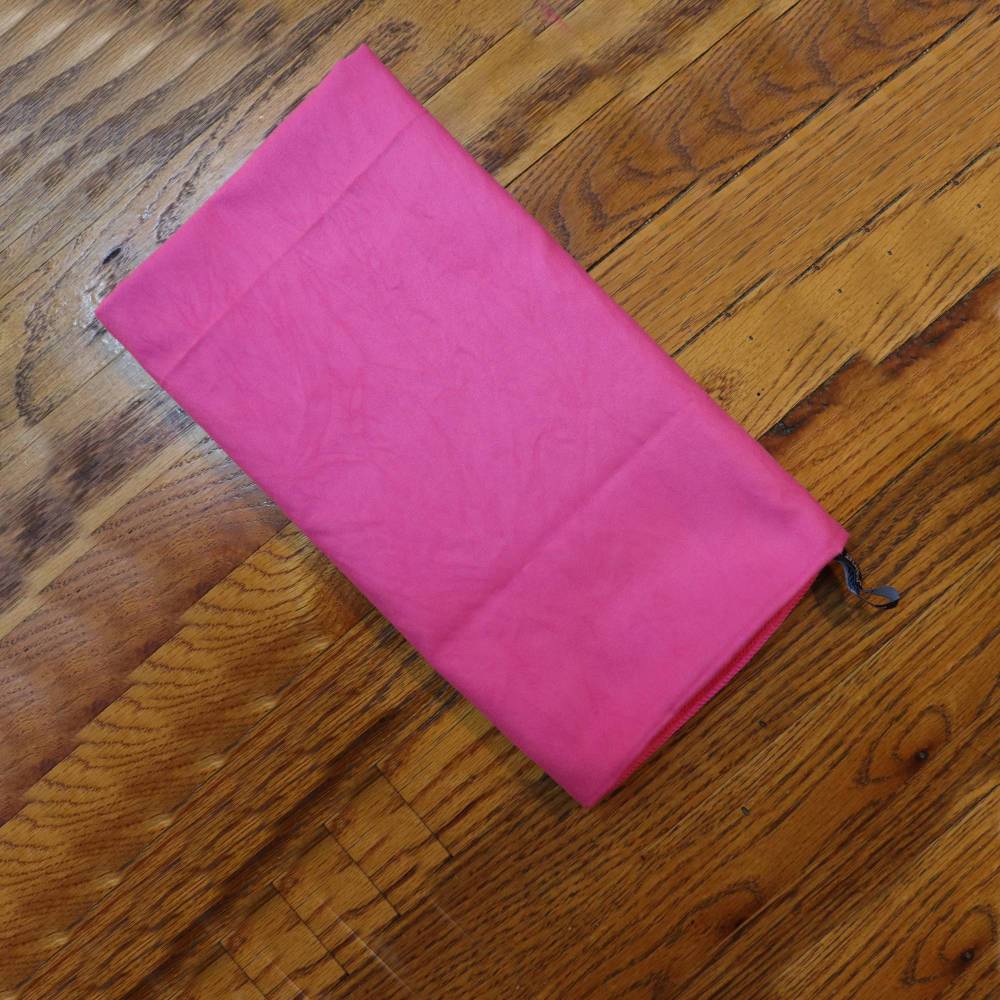 Pink microfiber towel folded on a wooden floor. Lightweight and absorbent, perfect for drying and caring for locs.