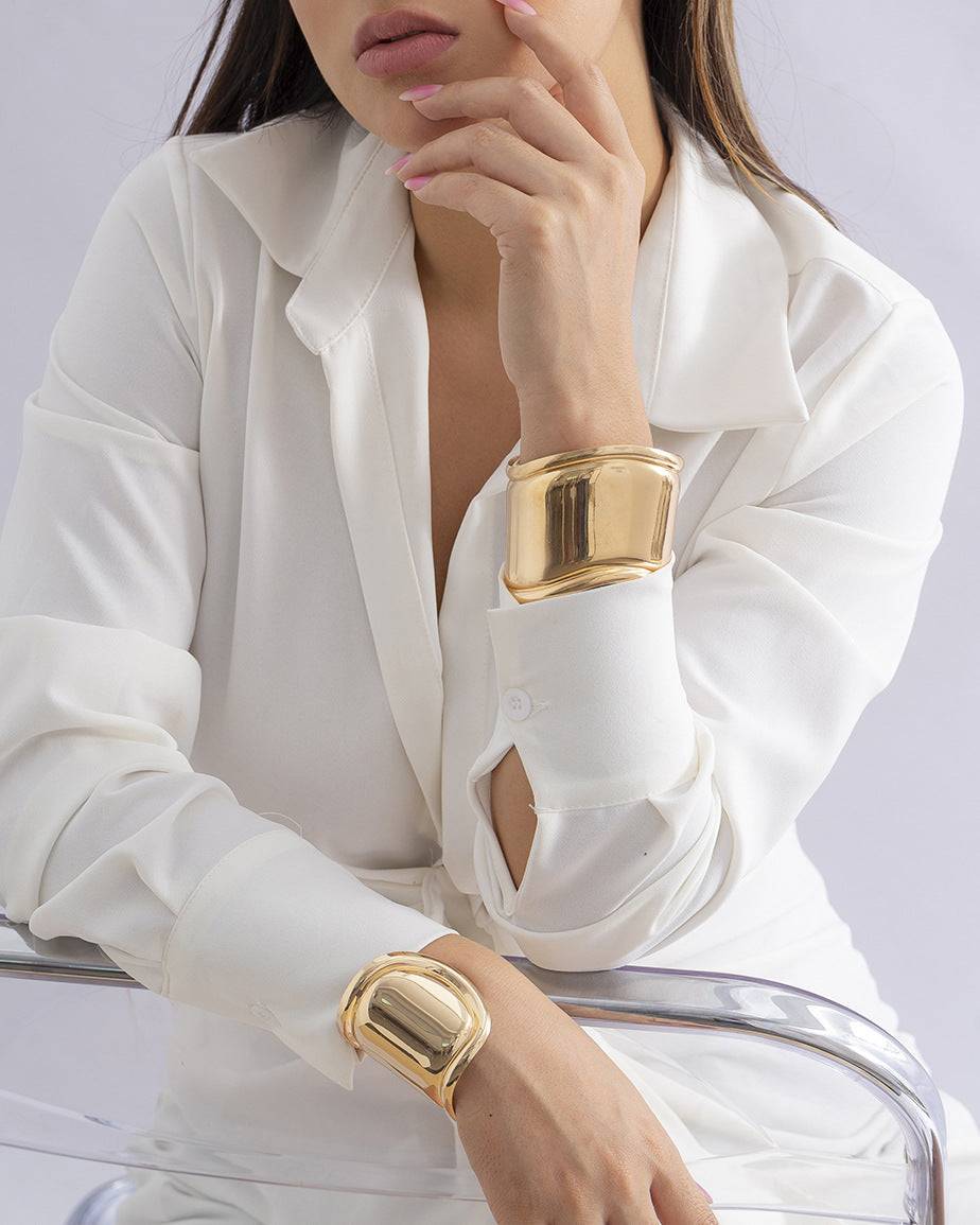 Model wearing two gold asymmetrical cuff bracelets with a white outfit. A bold fashion statement that also functions as a hair cuff for locs.