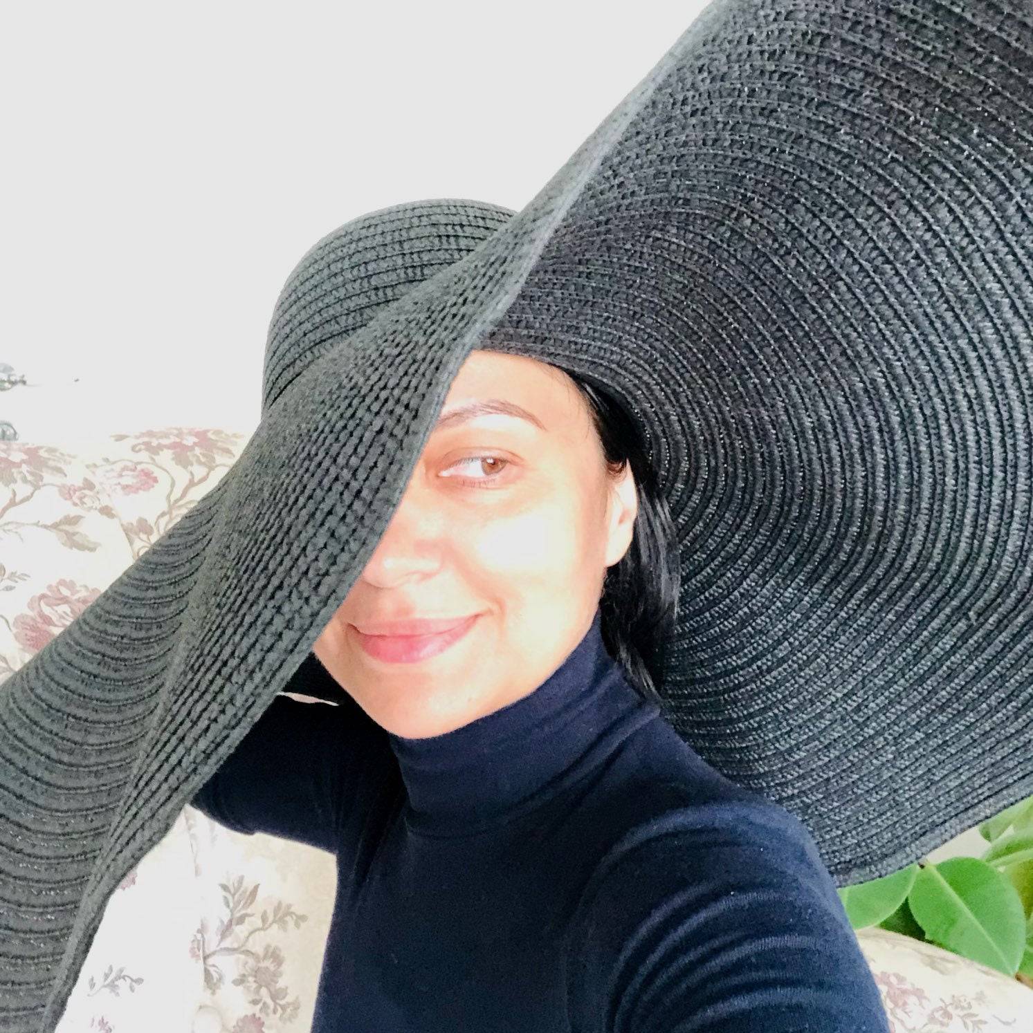 Smiling woman in a black oversized 27-inch wide brim sun hat, offering stylish sun protection for summer outings.