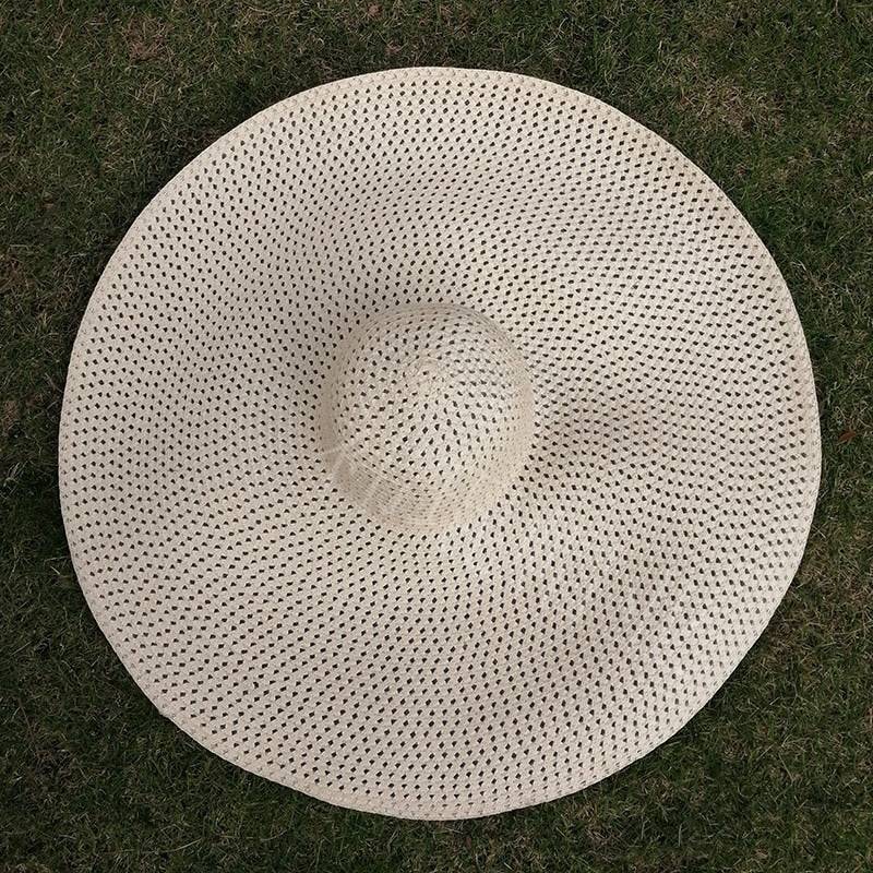 Natural woven oversized 27-inch wide brim sun hat on grass, breathable and stylish for summer.