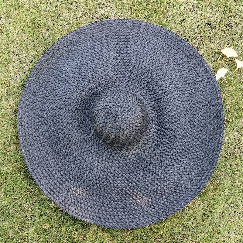 Black woven oversized 27-inch wide brim sun hat displayed on grass, offering breathable sun protection.
