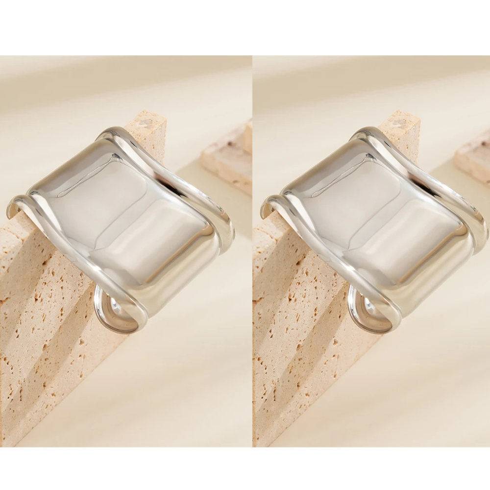 Pair of silver asymmetrical hair cuff bracelets displayed on a stone block. Stylish and non-damaging hair accessories for locs and dreadlocks.