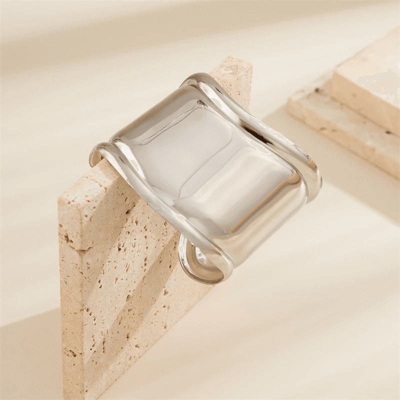 Silver asymmetrical hair cuff bracelet resting on a stone block. A chic and non-damaging hair accessory for locs and dreadlocks.