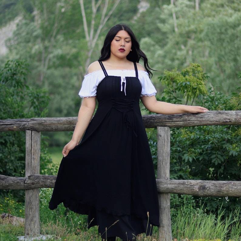 Black lace-up front maxi dress with elasticized back, worn with a white off-shoulder blouse in a rustic outdoor setting.