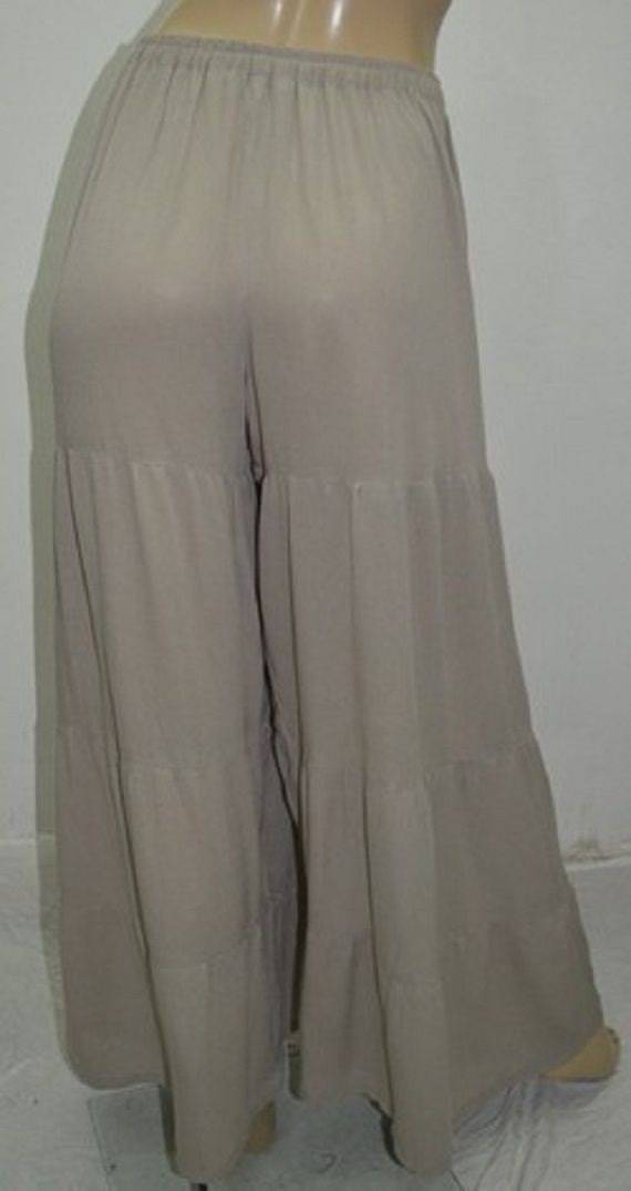 Back view of beige wide-leg pants with ruffled tiers. Lightweight and flowy fabric for a relaxed and stylish look.