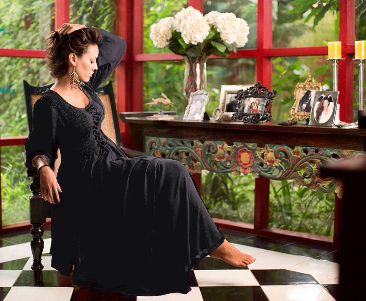 Black Renaissance-style maxi dress with smocked bodice and flowing skirt, worn in an elegant vintage-inspired interior setting.
