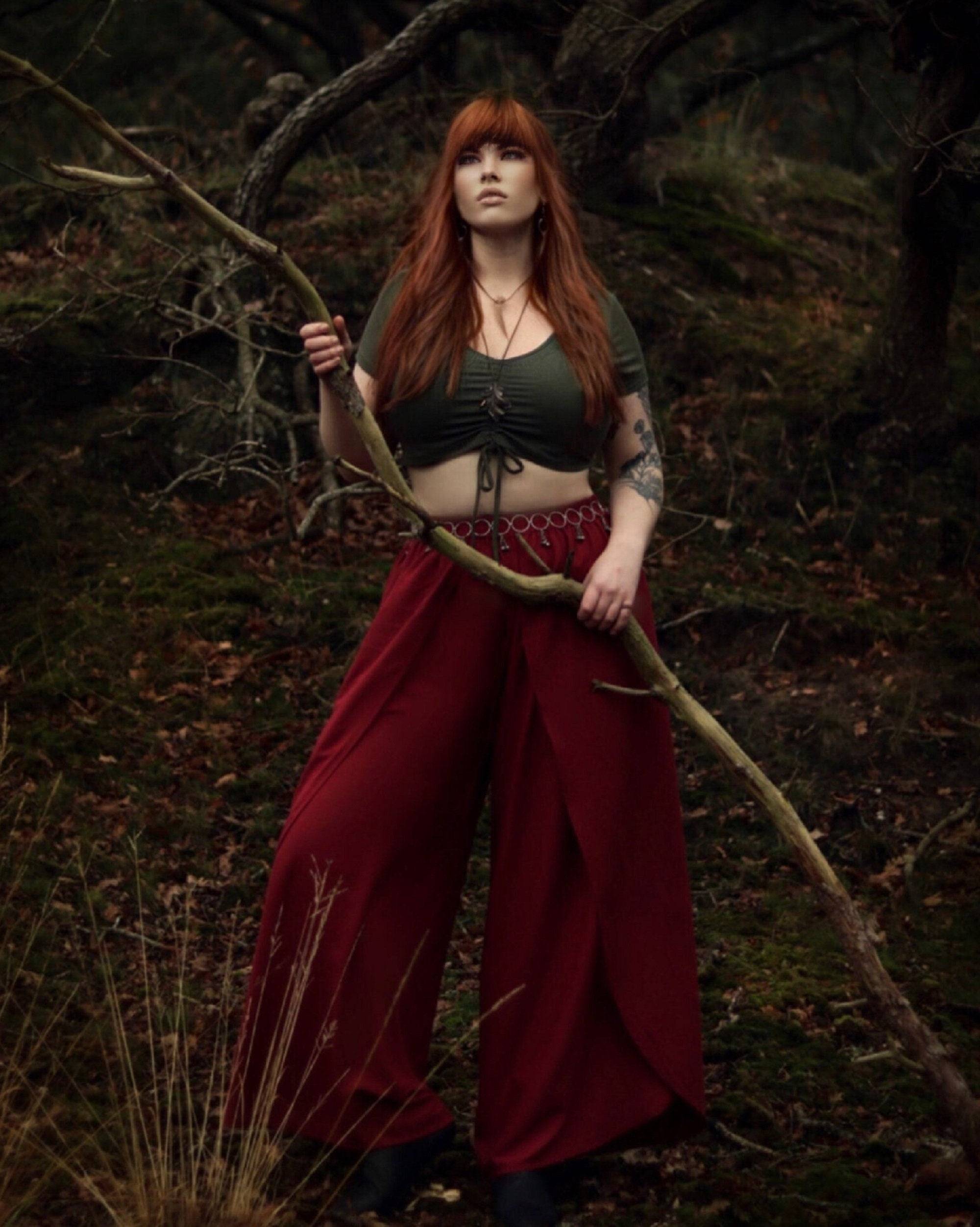 Woman wearing full-length layered pants with an elastic waist in deep red, styled with a crop top in a forest setting.