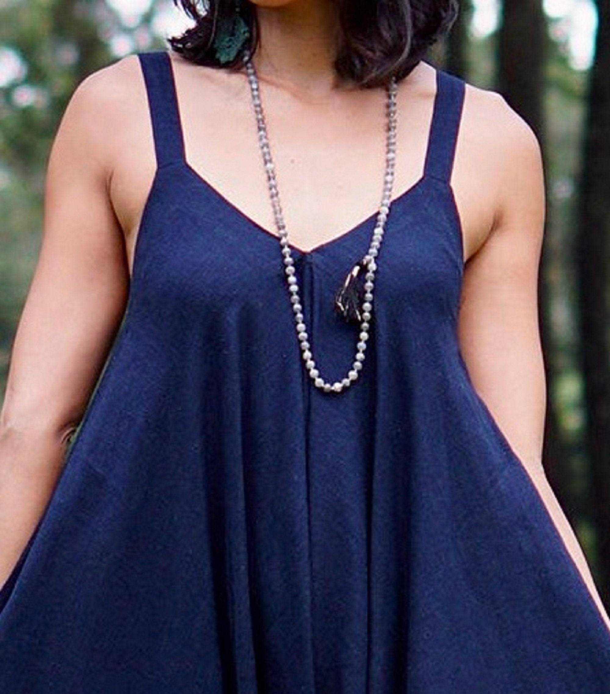 Close-up of a navy blue spaghetti angled straps jumpsuit with loose leg, accessorized with a beaded necklace for a boho-chic look.