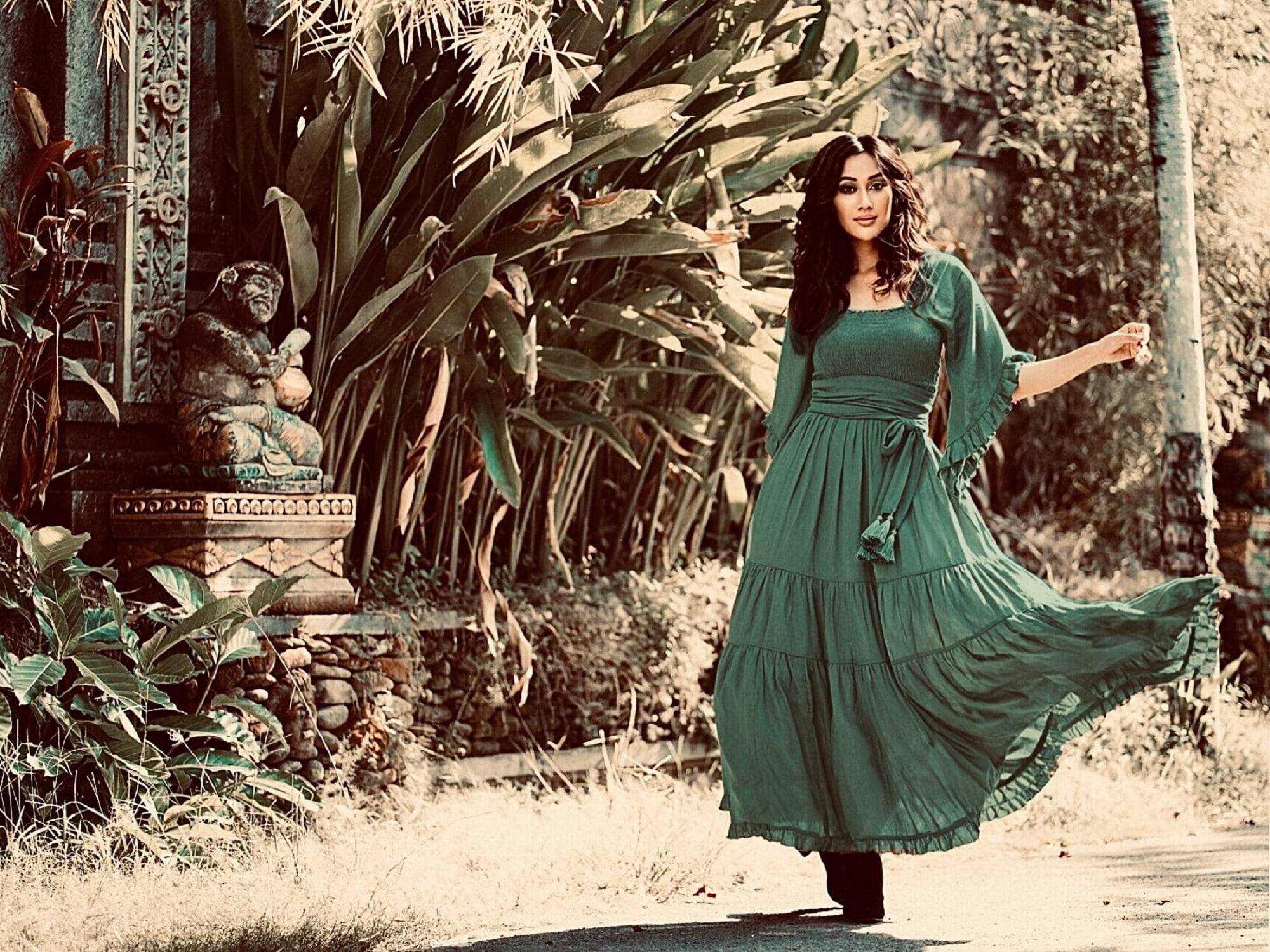 Emerald green medieval vintage maxi dress with an elasticized empire waist and tassel belt, flowing beautifully in a lush garden. A stunning boho-inspired outfit.