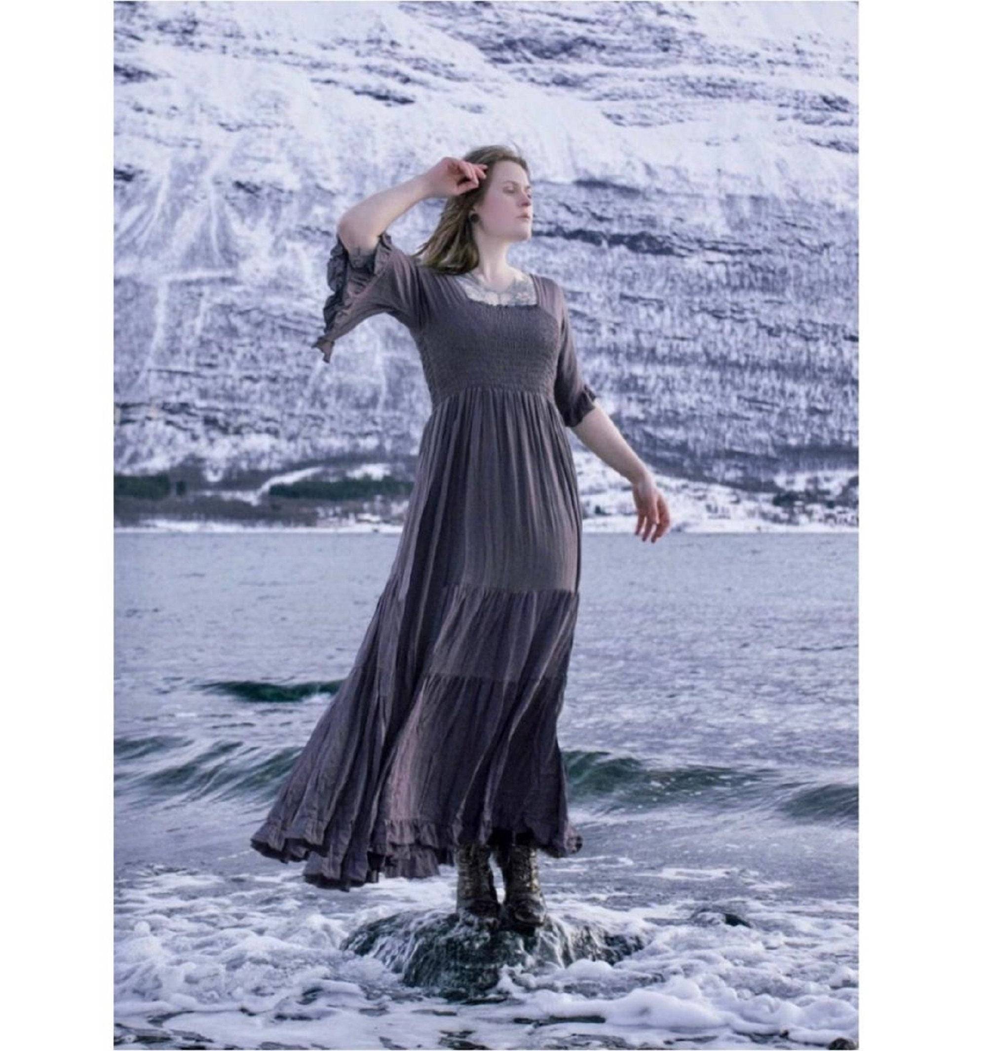 Gray medieval vintage maxi dress with an elasticized empire waist and tassel belt, worn in a dramatic icy landscape. A perfect blend of elegance and fantasy.