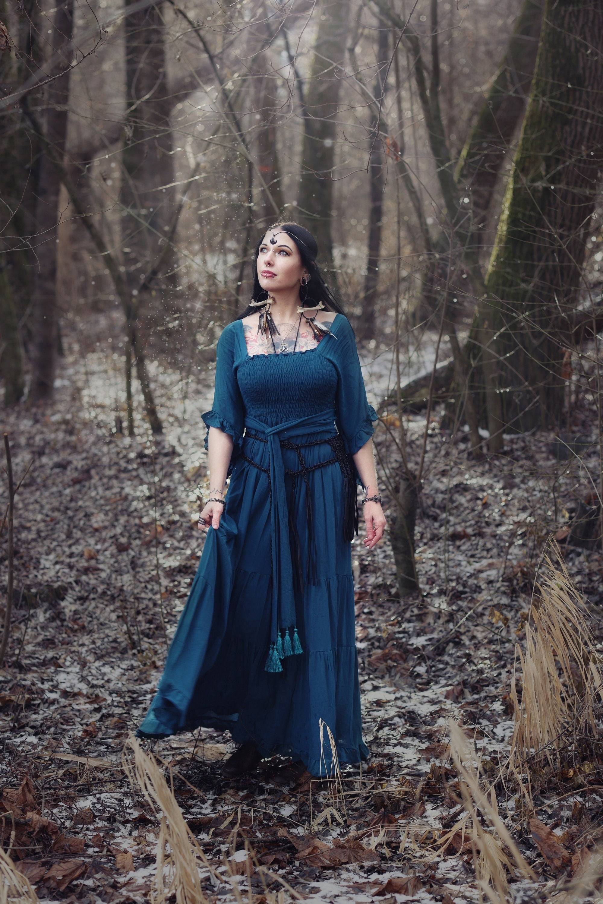 Dark blue medieval vintage maxi dress with an elasticized empire waist and tassel belt, styled in a mystical forest setting. Ideal for boho and fantasy looks.
