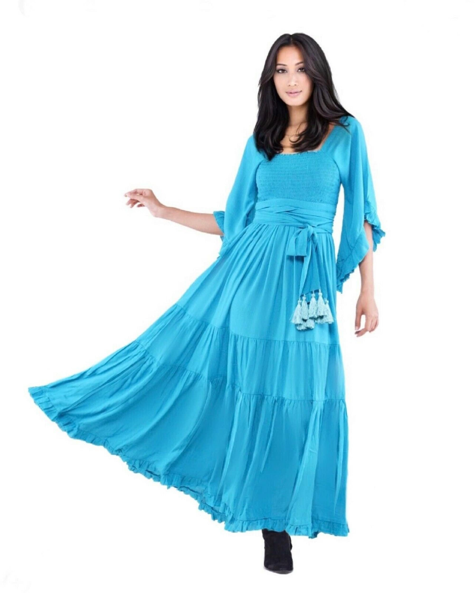 Bright turquoise medieval vintage maxi dress with an elasticized empire waist and tassel belt, styled against a white backdrop. A vibrant and elegant boho dress.