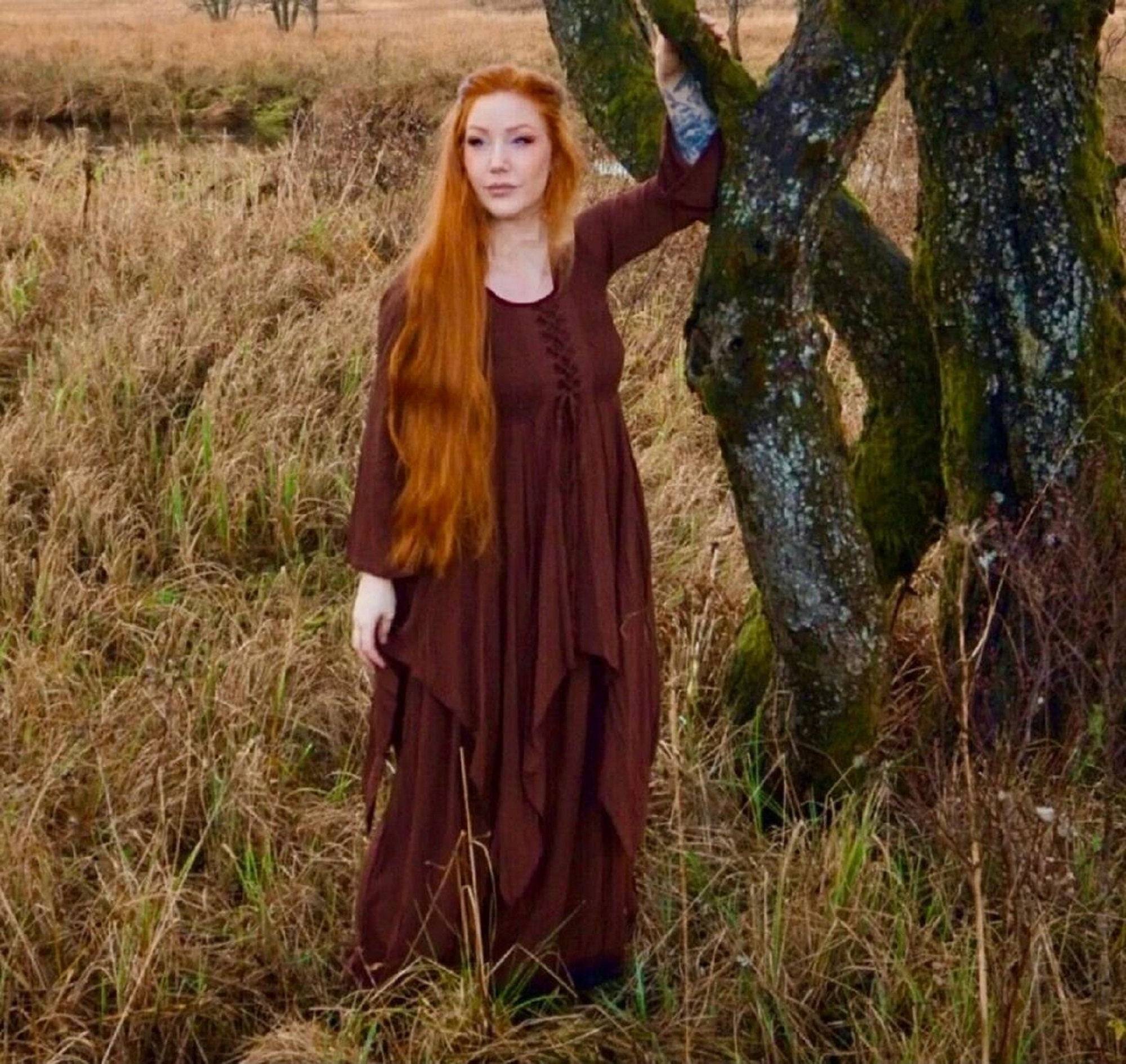 Earthy brown Renaissance maxi dress with layered skirt and lace-up bodice, styled in a rustic outdoor setting for a medieval or boho aesthetic.