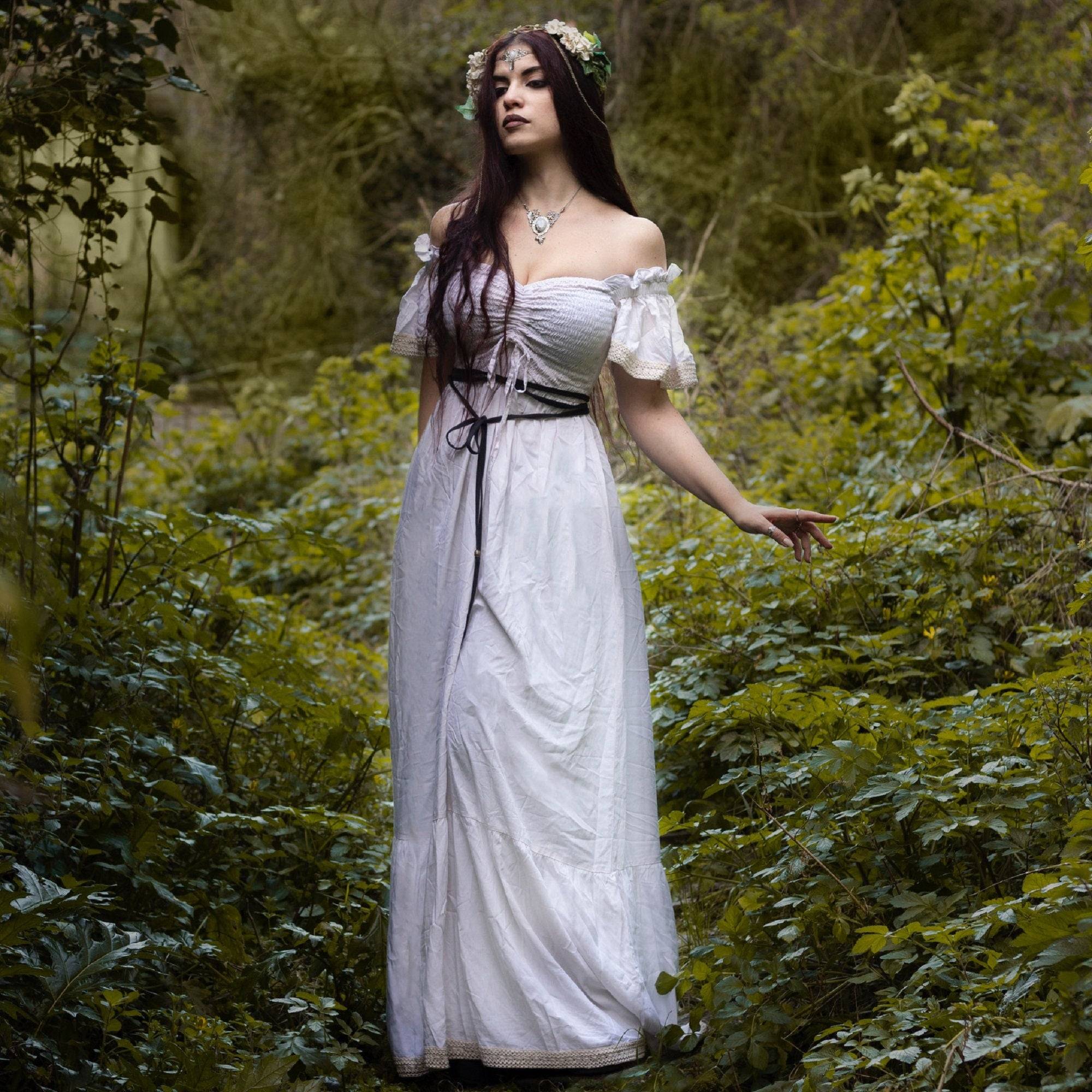 Elegant white maxi dress with smocked bust and ruffle lace trim, worn in a nature-inspired setting for a dreamy, ethereal look.