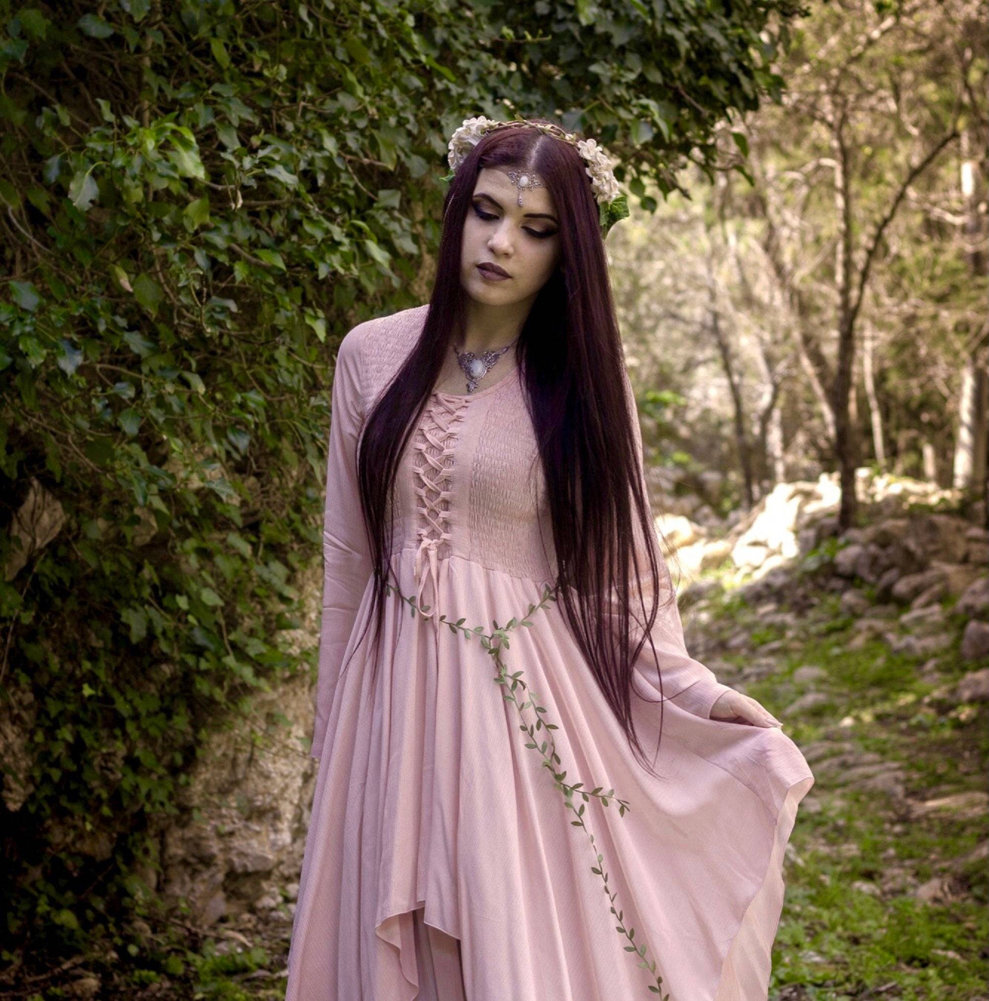 Soft pink Renaissance maxi dress with lace-up bodice and layered skirt, styled with floral accessories for a dreamy, fairy-tale aesthetic.
