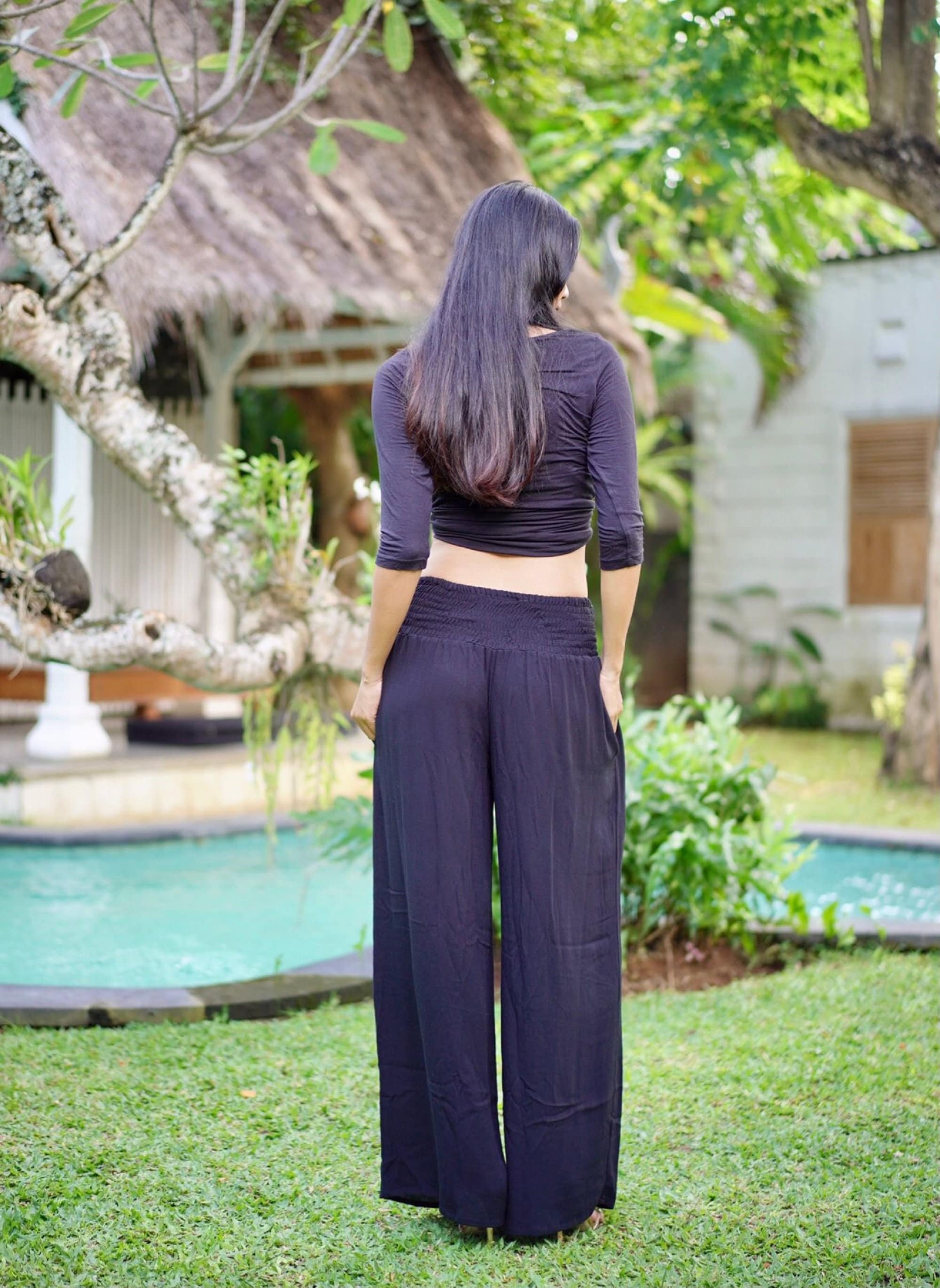 Back view of black wide leg palazzo pants with a smocked waist, showcasing a relaxed and elegant fit. Available in sizes S-5X.