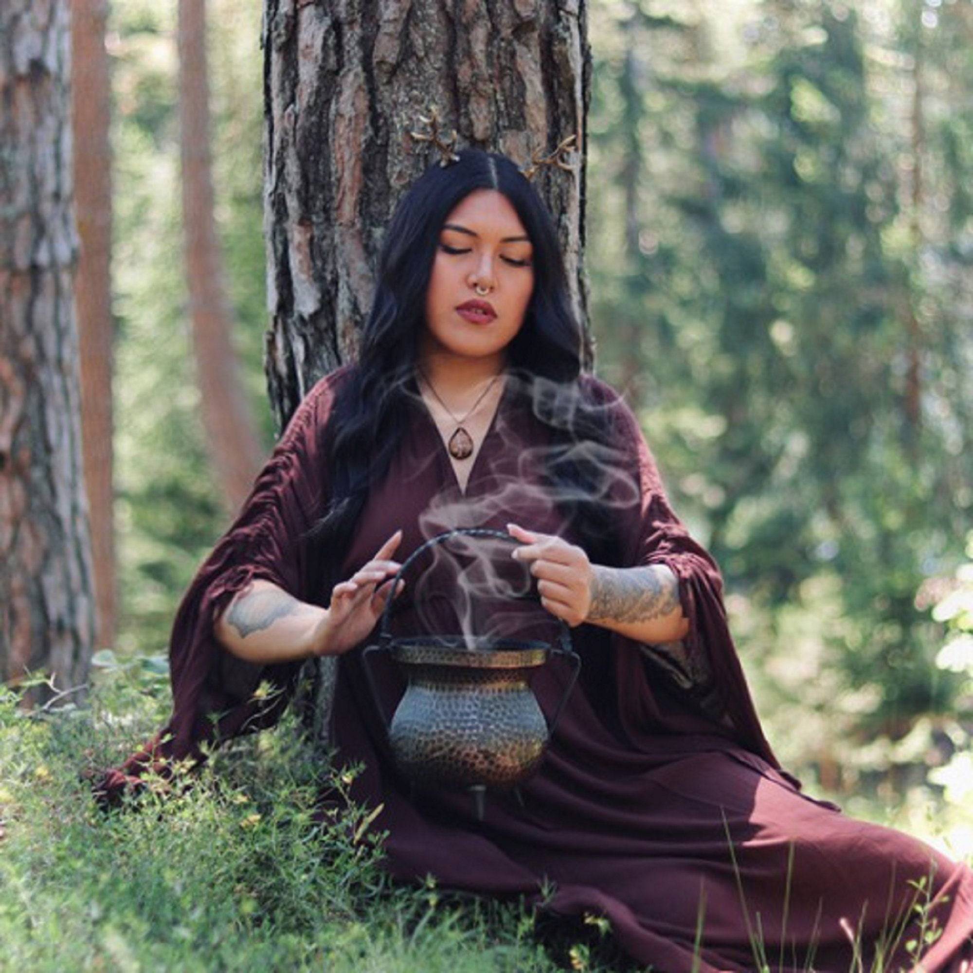 Mystical brown ruched gypsy gown with empire waist, worn in a forest while performing a ritual with a smoking cauldron. Ideal for boho aesthetics.