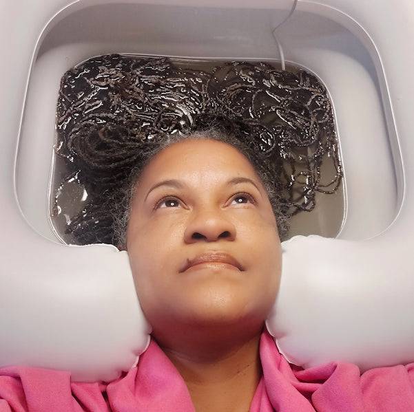 Close-up of a woman using the Sonic Loc Detox Rod in an inflatable basin, effectively removing buildup from locs.