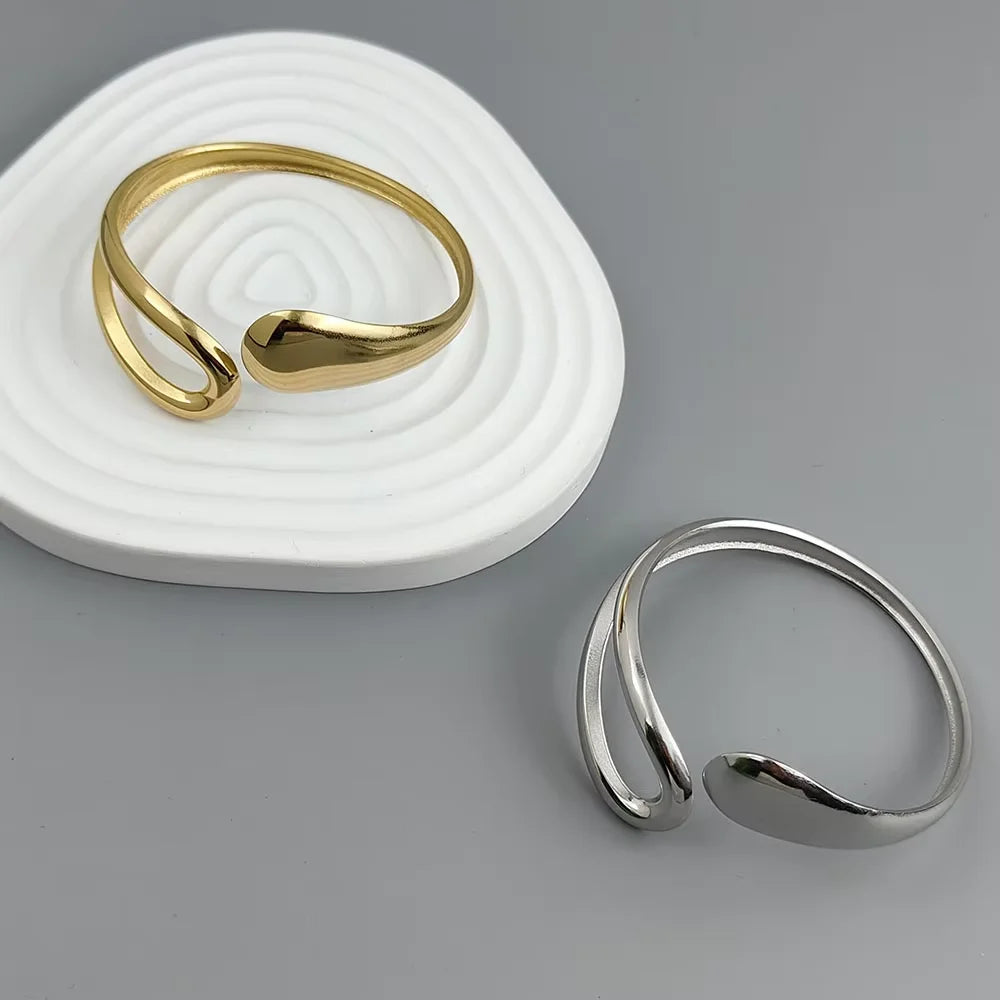 Adjustable gold and silver-plated cuff ring with modern minimalist open loop design on a gray background