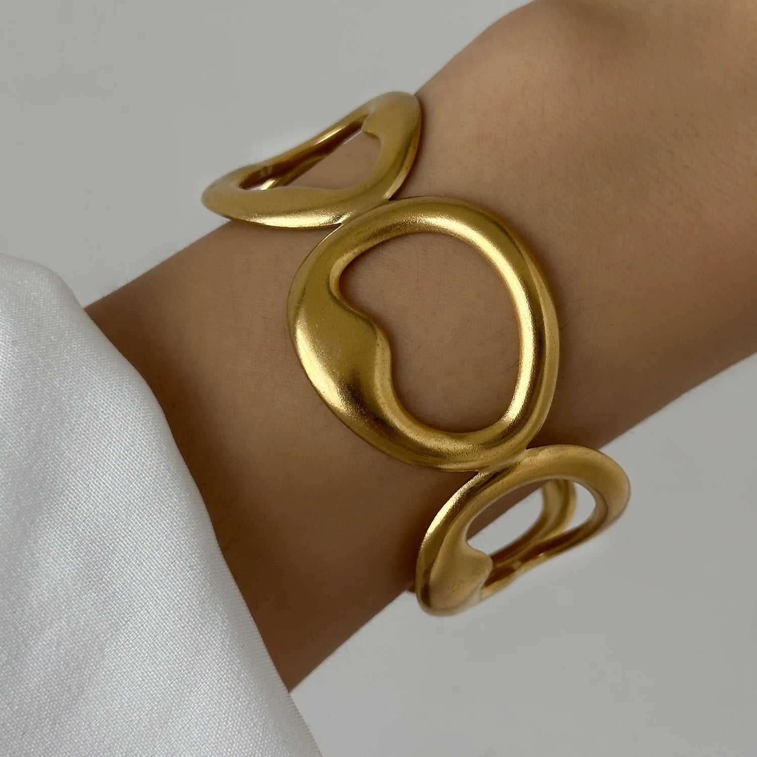 Close-up of a gold hollow cuff bracelet with abstract round shapes, worn on a wrist for a modern statement look