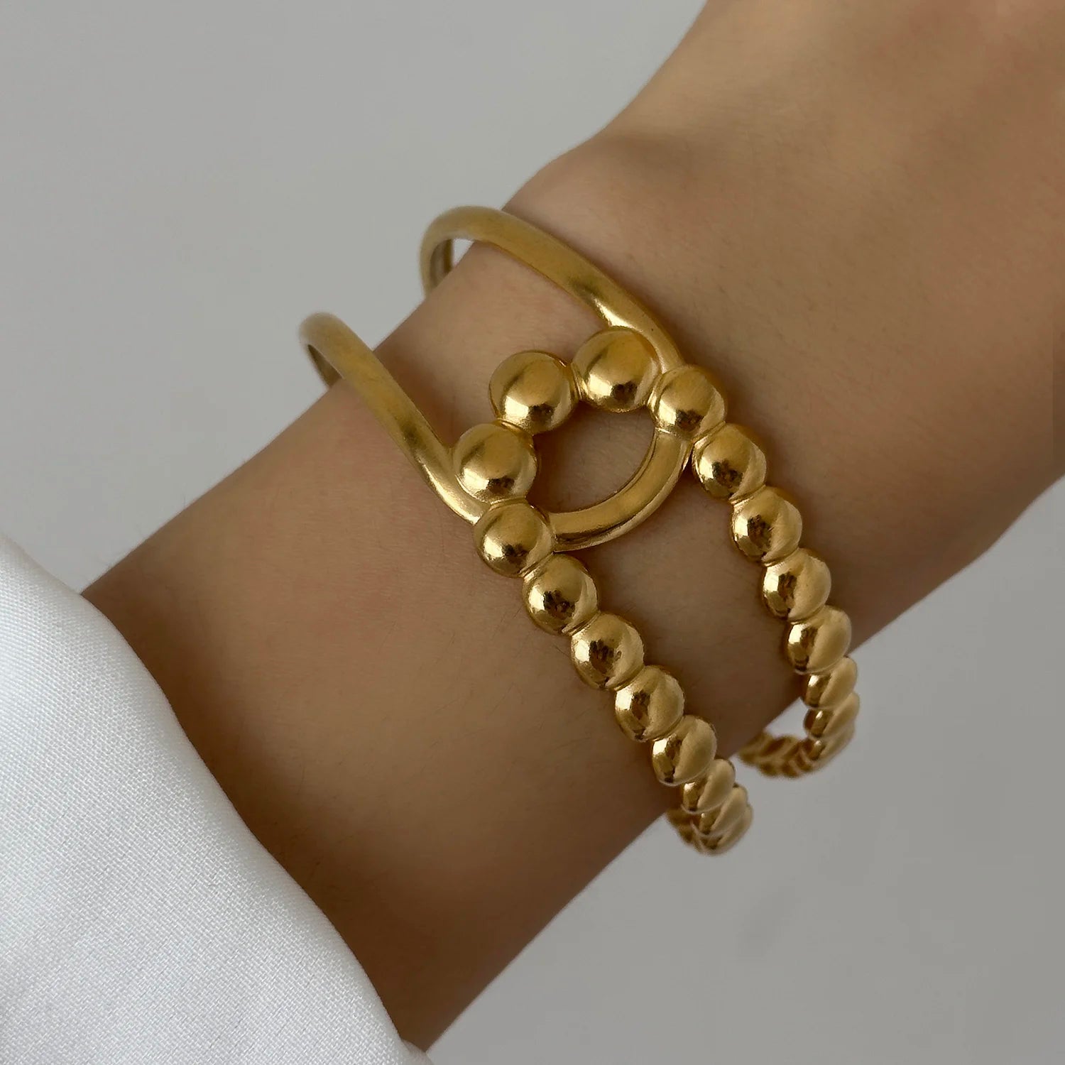 Gold beaded cuff bracelet with round decorative design, worn on wrist for a modern minimalist look