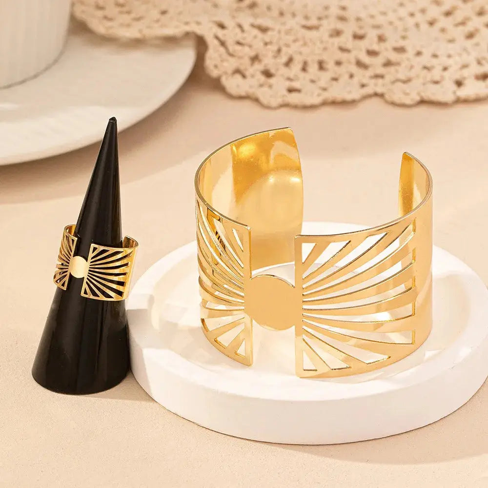Gold cut-out geometric bracelet displayed on a dish with matching ring on holder, showing intricate design details