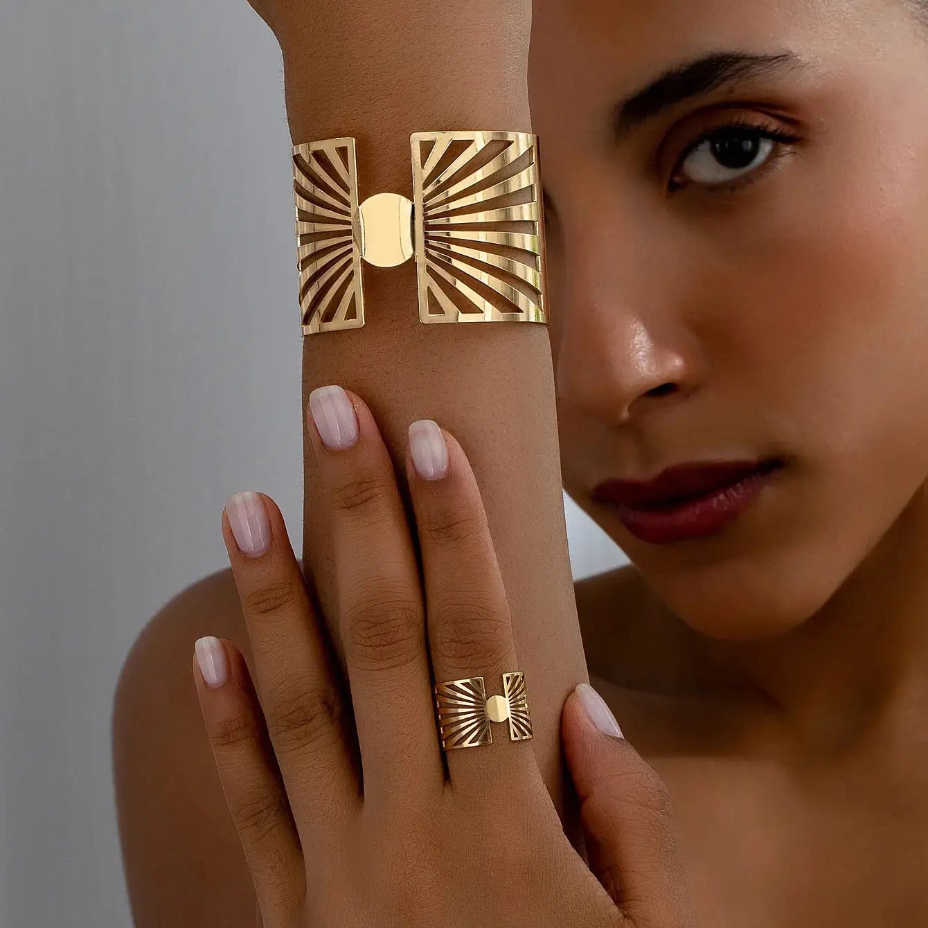 Close-up of a model wearing a gold geometric cut-out bracelet and matching ring, showing the elegant design on wrist and finger